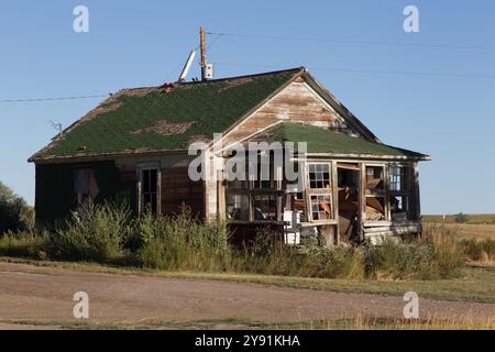 La vernice sbucciata, le finestre rotte, le scintille mancanti e il camino collassato segnano questa casa abbandonata ora utilizzata per lo stoccaggio della spazzatura, a sud di Simms, Montana. Foto Stock