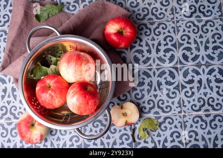 Le mele rosse mature giacciono in un colino metallico su un tavolo. Foto Stock