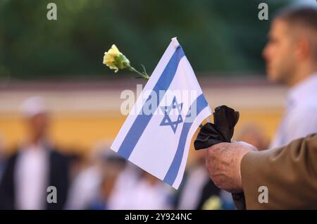Dettagli con le mani di un uomo che regge la bandiera israeliana e un fiore durante una cerimonia commemorativa degli attacchi dell'ottobre 2023. Foto Stock