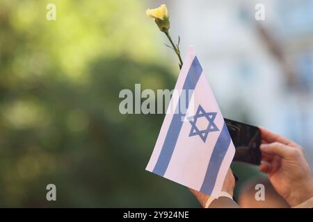 Dettagli con le mani di un uomo che regge la bandiera israeliana e un fiore durante una cerimonia commemorativa degli attacchi dell'ottobre 2023. Foto Stock