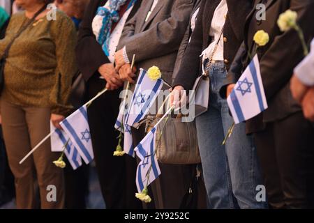 Dettagli con le mani di un uomo che regge la bandiera israeliana e un fiore durante una cerimonia commemorativa degli attacchi dell'ottobre 2023. Foto Stock
