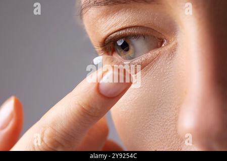 Una giovane donna mette la lente a contatto negli occhi su sfondo bianco. Occhiali, vista e visione, cura e salute degli occhi, oftalmologia e optometria concetto Foto Stock