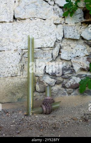 Tubo in vetro verdastro con raccordo arrugginito vicino a parete in pietra grigia Foto Stock