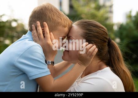 Un momento amorevole tra madre e figlio in un parco soleggiato, in cui condividono un tocco giocoso di fronte e sorrisi Foto Stock