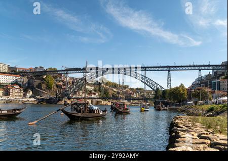 Porto, Portogallo - 12 settembre 2024: Barche colorate scivolano lungo il fiume mentre l'iconico ponte domina lo skyline. Foto Stock