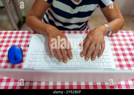 Le mani degli anziani sulla tastiera del notebook con mouse blu: Imparare la tecnologia a casa Foto Stock