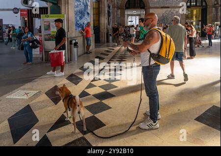 Porto, Portogallo - 12 settembre 2024: Un uomo con uno zaino cammina con il suo cane mentre si gode un'atmosfera vivace della stazione ferroviaria. Foto Stock