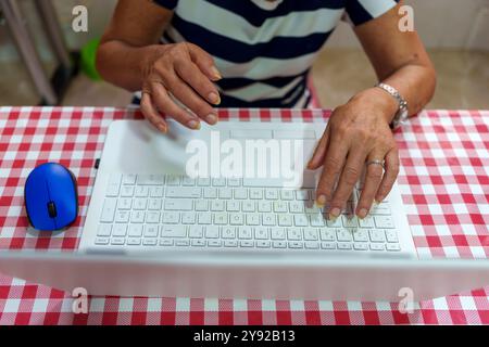 Le mani degli anziani sulla tastiera del notebook con mouse blu: Imparare la tecnologia a casa Foto Stock