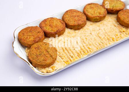 Polpettine di falafel croccanti su un morbido letto di hummus in un piatto bianco, primo piano della cucina mediorientale Foto Stock