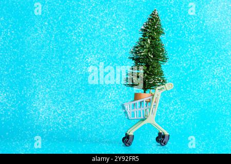 Mini albero di Natale in un piccolo carrello giocattolo, caratterizzato da uno sfondo blu brillante con effetti simili alla neve, perfetto per l'arredamento delle feste. Foto Stock