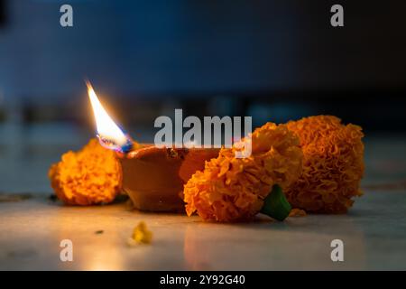 Una lampada di fango in fiamme (diya) circondata da fiori vibranti durante Navratri, un festival indù che celebra le dee indiane. Catturato a Uttarakhand, India. Foto Stock