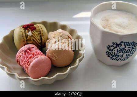 Tazza di caffè bianco e macaron in diversi colori e gusti nel piatto beige Foto Stock