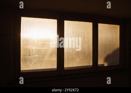 La calda luce del sole del mattino filtra attraverso una finestra smerigliata, diffondendo ombre e luci soffuse nell'edificio di appartamenti. Una rappresentazione serena di un inizio pacifico Foto Stock