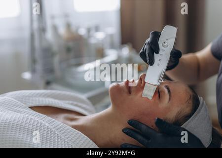 Cosmetologo che effettua il trattamento del viso con spatola a ultrasuoni per giovani donne. . Foto di alta qualità Foto Stock