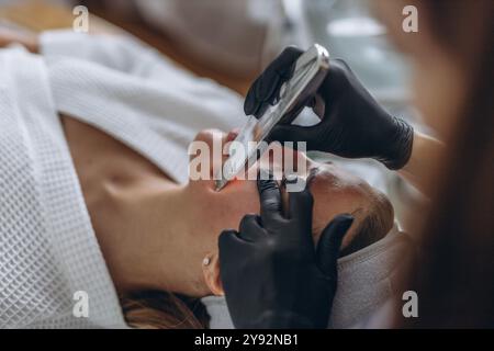 Cosmetologo che effettua il trattamento del viso con spatola a ultrasuoni per giovani donne. Foto Stock