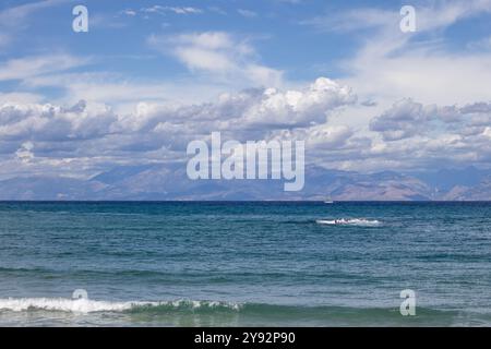 Acque blu del Mar Ionio nella parte nord-orientale dell'isola. Montagne in Albania all'orizzonte. Cielo blu con nuvole bianche. Agios Spyridon, Co Foto Stock