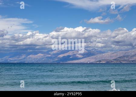 Acque blu del Mar Ionio nella parte nord-orientale dell'isola. Montagne in Albania all'orizzonte. Cielo blu con nuvole bianche. Agios Spyridon, Co Foto Stock