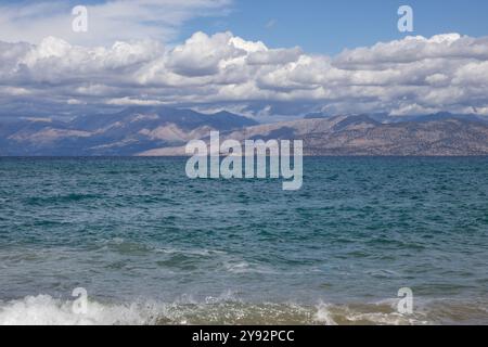 Acque blu del Mar Ionio nella parte nord-orientale dell'isola. Montagne in Albania all'orizzonte. Cielo blu con nuvole bianche. Agios Spyridon, Co Foto Stock