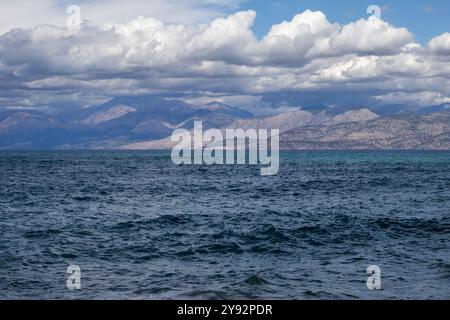 Acque blu del Mar Ionio nella parte nord-orientale dell'isola. Montagne in Albania all'orizzonte. Cielo blu con nuvole bianche. Agios Spyridon, Co Foto Stock