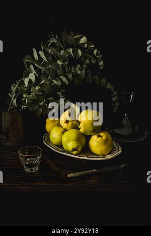 Una drammatica natura morta caratterizzata da principi appena raccolti e un vaso con rami di eucalipto, catturati con un'illuminazione chiaroscuro a basso volume, che crea un ricco Foto Stock