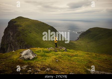 Un'escursionista solitaria si erge su una pittoresca montagna che offre vedute mozzafiato del mare Foto Stock