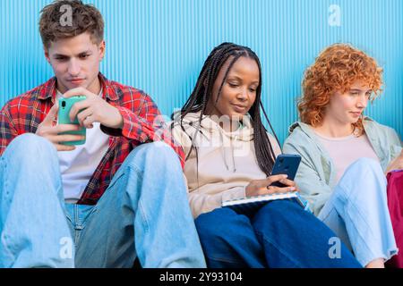 Diversi giovani seduti all'aperto con smartphone Foto Stock