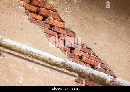 Parete danneggiata in mattoni rossi con stucco giallo, texture fotografica di sfondo Foto Stock