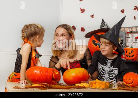 La famiglia si diverte ad Halloween intagliando le zucche insieme a tavola Foto Stock