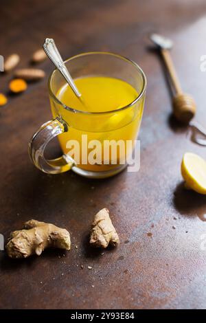 Immunitaria Boosting inverno rimedio bevanda calda con curcuma, zenzero, limone e miele. Tazza con bevanda calda e ingredienti su sfondo scuro. Foto Stock