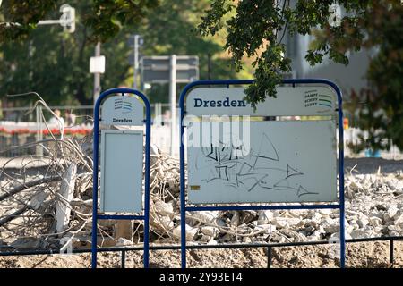 Dresda, Germania. 8 ottobre 2024. Una bacheca informativa vuota del Sächsische Dampfschifffahrt con l'iscrizione "Dresda" si trova di fronte a parti del ponte Carola crollato sul lato della città Vecchia dell'Elba. Tre settimane dopo il crollo parziale del Ponte Carola di Dresda, i lavori di demolizione e la ricerca delle cause continuano. Crediti: Sebastian Kahnert/dpa/Alamy Live News Foto Stock