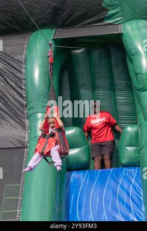 Sotto un occhio vigile, la giovane ragazza un po' spaventata cavalca la zip Line amazzonica alla festa del Putnam Valley Town Day del 2024 nella contea di Putnam, New York. Foto Stock