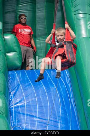 Sotto un occhio vigile, un giovane ragazzo cavalca la zip Line amazzonica durante la festa del Putnam Valley Town Day del 2024 nella contea di Putnam, New York Foto Stock