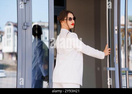 Elegante donna d'affari che esce dal moderno edificio per uffici con sicurezza e stile. Foto Stock