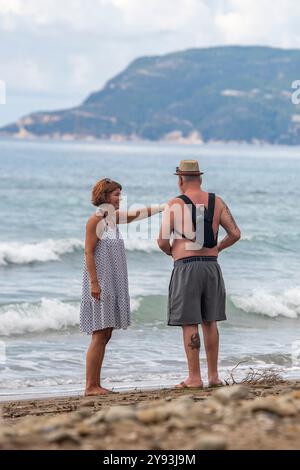 Coppia di mezza età che tiene una discussione in piedi sul bordo dell'acqua su una spiaggia in Grecia, signora che dà istruzioni a suo marito durante una discussione Foto Stock