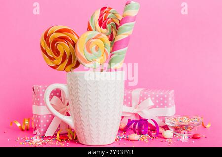 Caramelle colorate in tazza su tavolo su sfondo chiaro. Lecca-lecca grande e vorticosa. Concetto creativo di un vaso pieno di dolci deliziosi dal Foto Stock