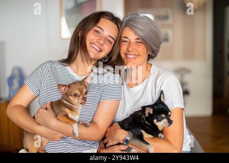 Una scena commovente di una madre e sua figlia, sorridenti e con due cani piccoli, che mostrano un'atmosfera familiare e accogliente i setti interni Foto Stock