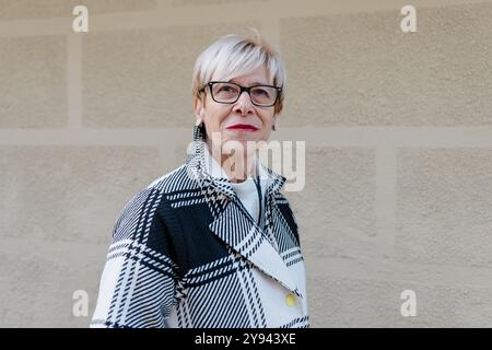 Un'elegante donna anziana con capelli biondi corti e occhiali eleganti sorride dolcemente alla macchina fotografica indossa un'elegante giacca a scacchi in bianco e nero sopra un Foto Stock