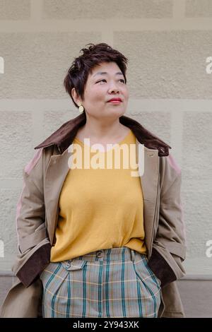Ritratto di una donna asiatica sicura di sé, in posa rilassata, sorridente delicatamente, indossa un vivace top giallo con un'elegante giacca a strati Foto Stock