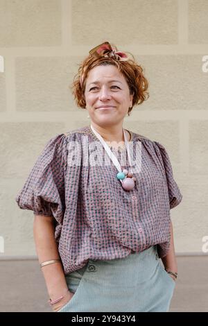 Ritratto di una donna di mezza età sorridente vestita con un abito elegante, in piedi con sicurezza davanti a una parete di mattoni dalle texture chiare, il suo aspetto sereno e felice Foto Stock