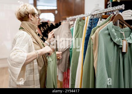 Due amiche sfogliano una collezione di abiti in una boutique, selezionano gli articoli e discutono delle loro scelte Foto Stock