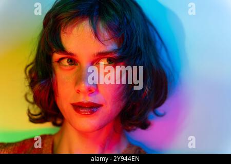Foto ravvicinata di una giovane donna immersa in una luce multicolore, che crea un effetto visivo vibrante e drammatico. Il suo sguardo misterioso si aggiunge agli intens Foto Stock