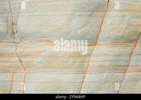Un primo piano della superficie di un arenaria, che mostra diverse texture e bande di colore dal verde pallido alla ruggine, con grana visibile e motivi di crepe ideali Foto Stock