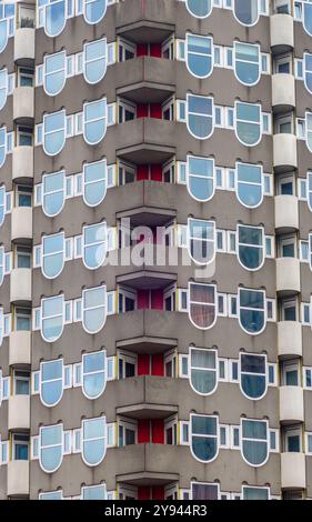 Primo piano architettonico di un edificio moderno a Rotterdam caratterizzato da una facciata adornata da finestre a forma di scudo e audaci elementi rossi Foto Stock