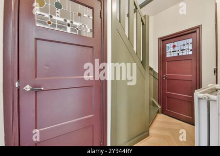 Invitante ingresso casa caratterizzato da una porta marrone con vetrate colorate, pavimenti in legno e una scala classica. Foto Stock