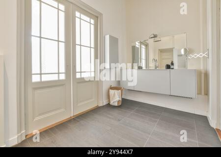 Un bagno spazioso e moderno con elegante lavandino bianco, grande specchio e illuminazione naturale dalle finestre a tutta altezza. Foto Stock