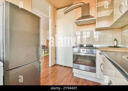 Questa immagine presenta una piccola cucina ben illuminata con moderni elettrodomestici in acciaio inossidabile, pavimento in legno e armadi color crema. Foto Stock