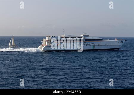 Il Jean de la Valette, un catamarano ad alta velocità passeggeri e traghetto per auto in partenza da Malta in transito verso la Sicilia passando per uno yacht a vela. Foto Stock