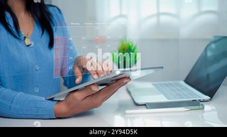 Donna d'affari che segna le date sul calendario virtuale con un tablet, gestisce il suo programma aziendale, imposta promemoria per appuntamenti importanti, co creativo Foto Stock