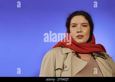 Una donna versatile e versatile sfoggia il suo stile con una sciarpa rossa e un trench dalle tonalità blu. Foto Stock