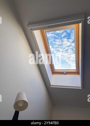 La vista del cielo limpido attraverso un lucernario rivela una serie di nuvole vibranti, offrendo un sereno scorcio all'aperto. La struttura in legno aggiunge calore e contrasto a. Foto Stock